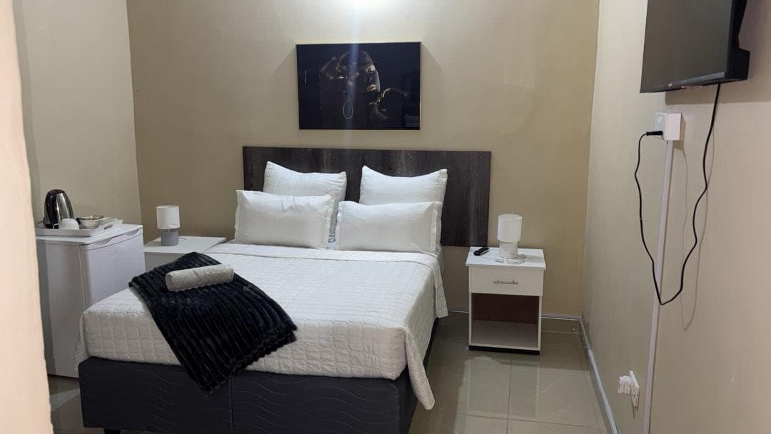 Double room at Fallsview Guest House with white bedding, bedside lamps, a wall-mounted TV and a tea and coffee tray