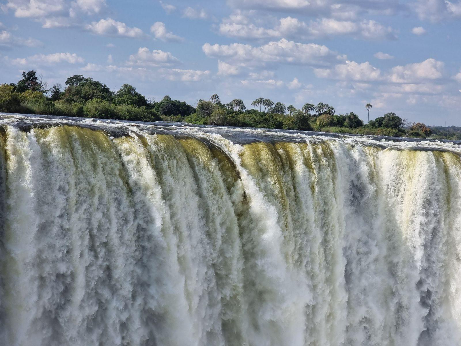 The Zambezi River flowing over the lip of Victoria Falls under a cloudy sky