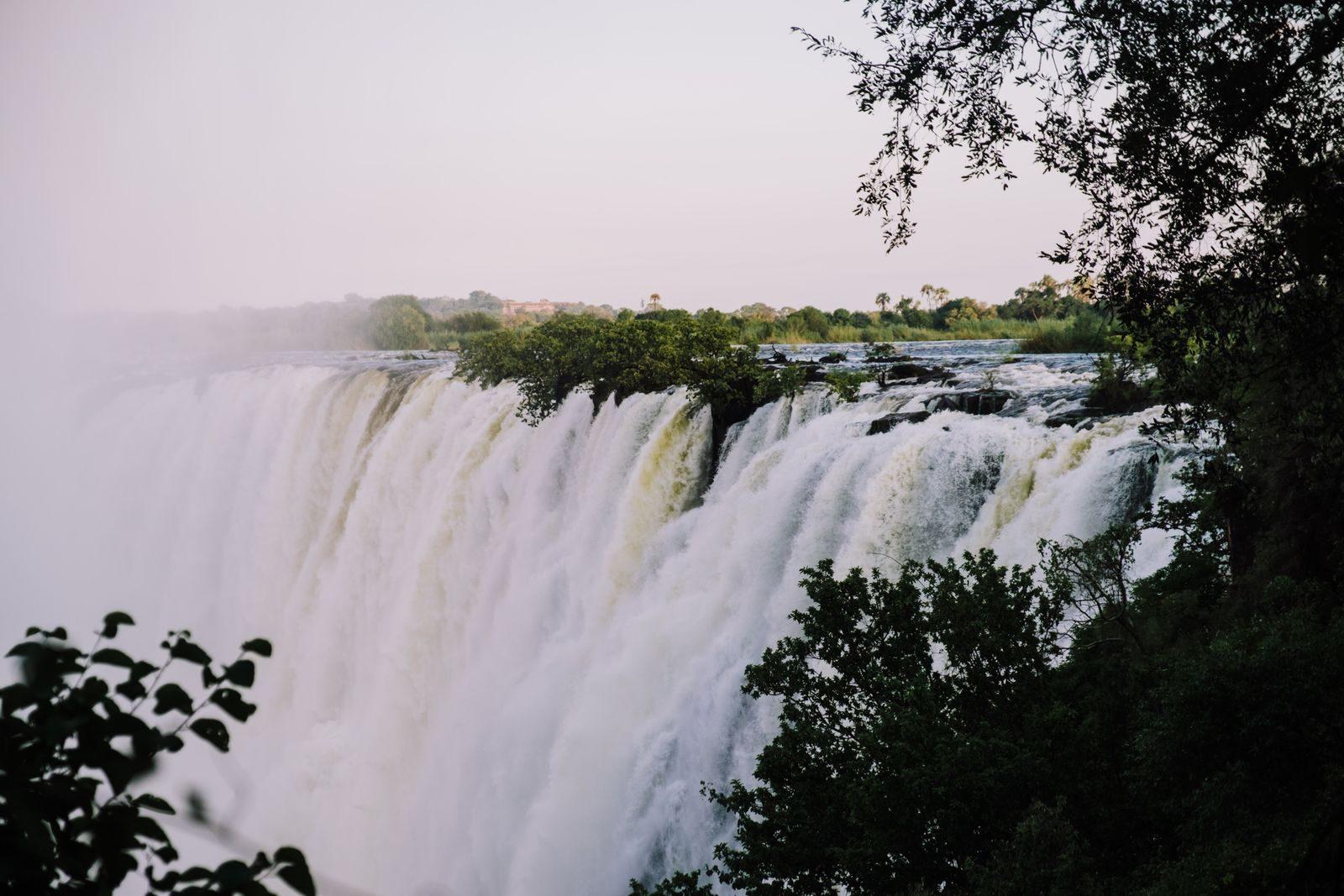 The main curtain of Victoria Falls framed by trees, with spray rising from the gorge