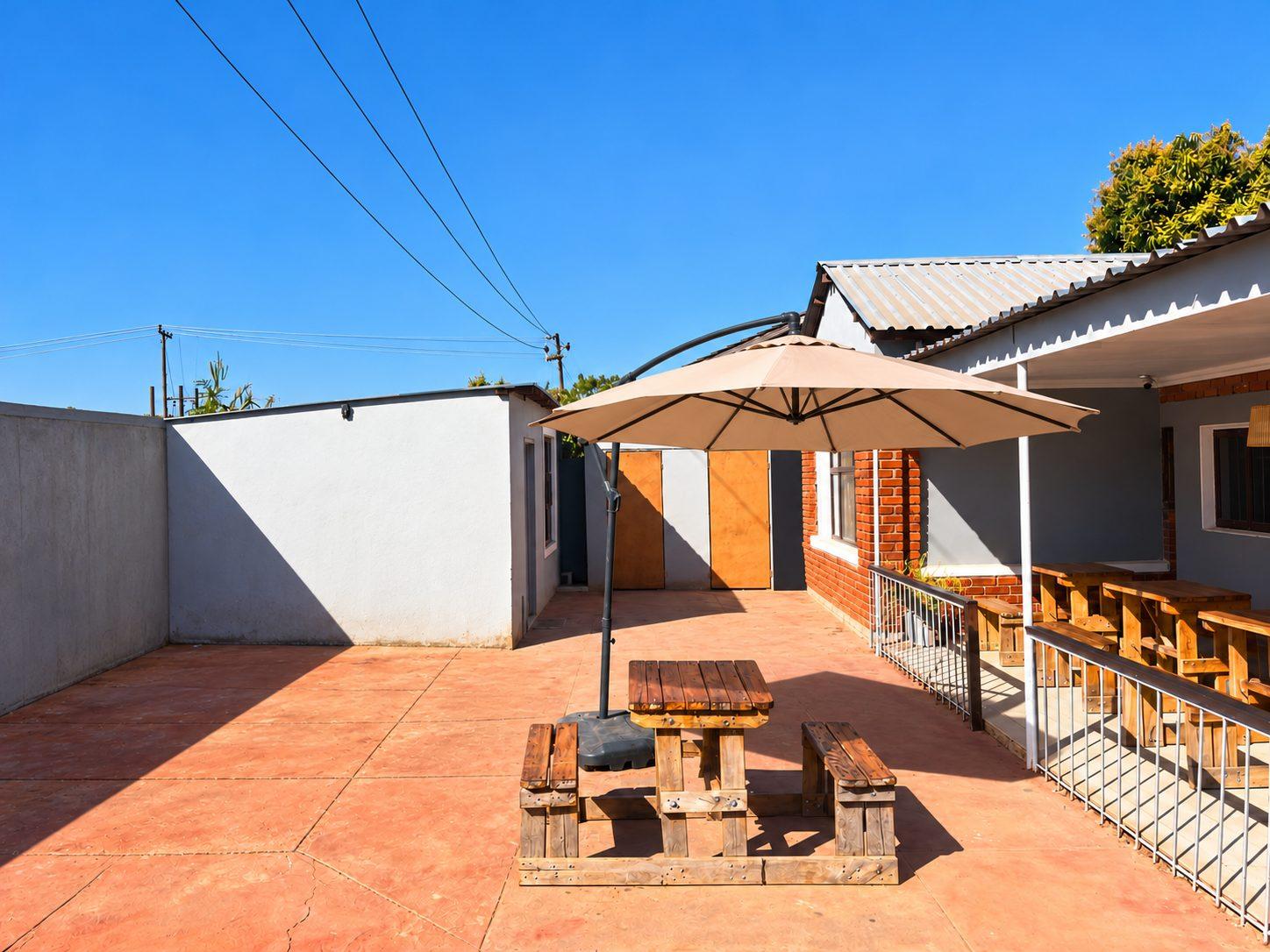 Paved courtyard with a wooden picnic table under a large umbrella at Fallsview Guest House