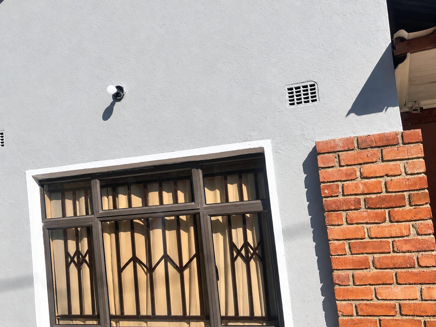 Grey rendered wall with a burglar-barred window and a face-brick pillar at Fallsview Guest House