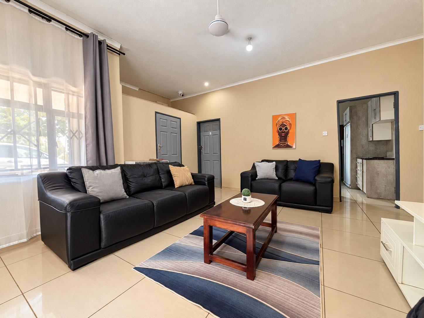 Lounge at Fallsview Guest House with black leather sofas, a coffee table and a doorway through to a kitchen