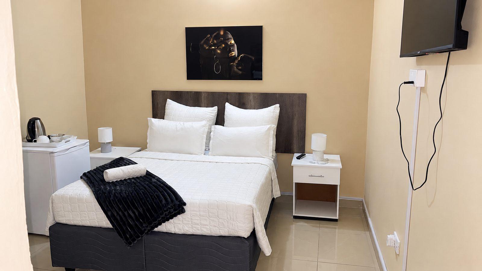 Standard double room at Fallsview Guest House with white bedding, bedside lamps, a wall-mounted TV, a bar fridge and a tea and coffee tray