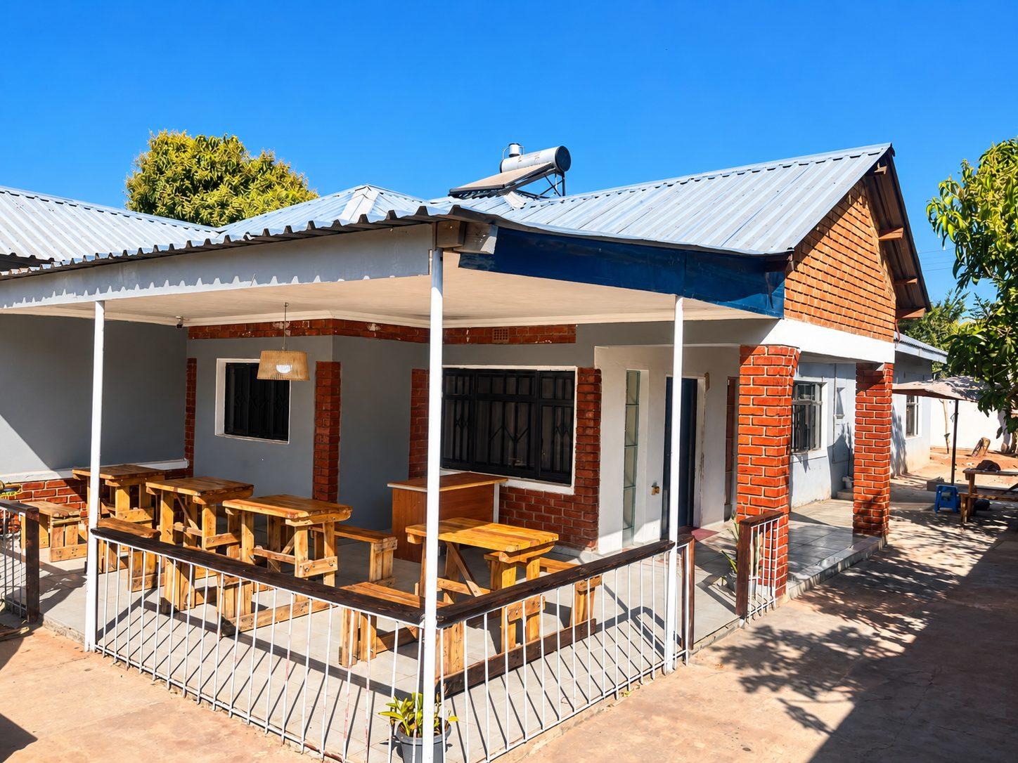Covered veranda with wooden dining tables beside the face-brick main building at Fallsview Guest House on a sunny day