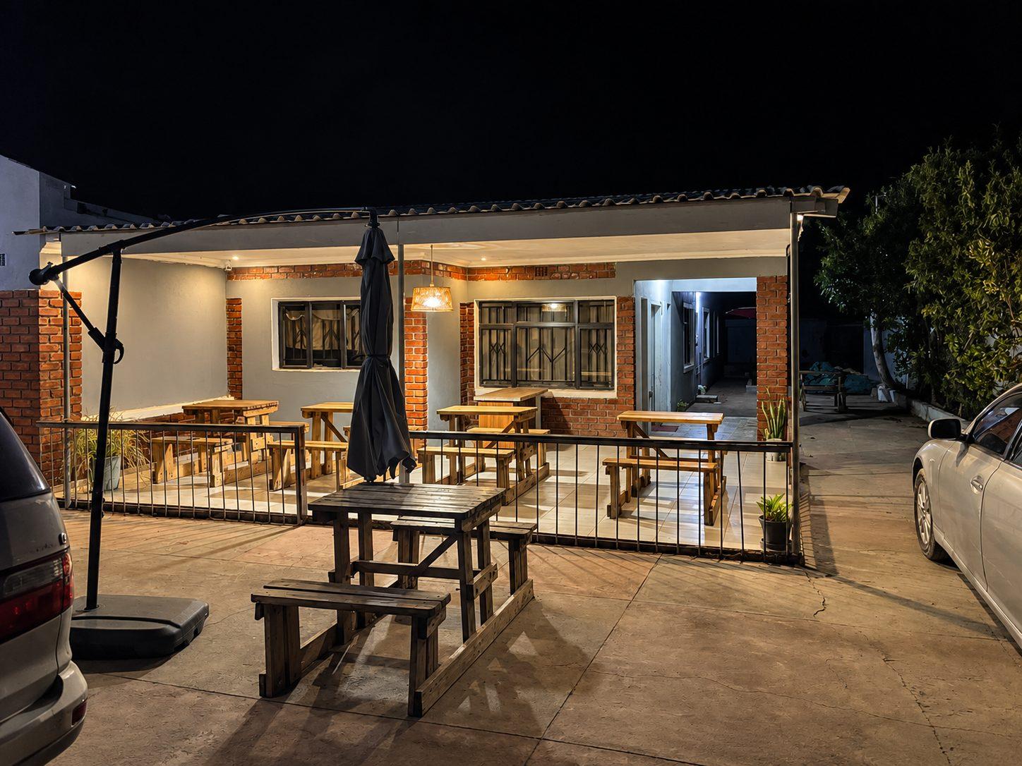 The veranda dining area at Fallsview Guest House lit up at night, with wooden tables and cars parked in the courtyard